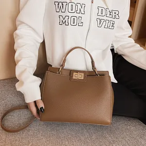 Detail of a brown lychee pattern leather handbag with a gold twist lock and long strap