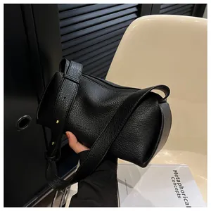 Close-up of black textured leather bag featuring a wide strap and golden metal buckle
