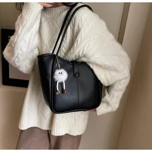 Close-up of black tote bag with vertical stitching and a plush monster charm detail