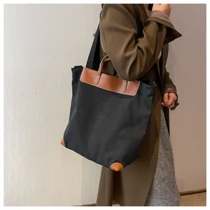 Detail of a large black canvas tote bag with brown leather trim and fabric shoulder strap