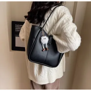 Detail of a black leather tote bag with a white monster charm and slender shoulder straps