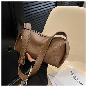 Detail of a brown textured cylinder bag with wide strap and gold hardware buckles