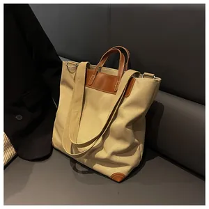 Detail view of large canvas tote bag with brown leather trim on a grey leather sofa