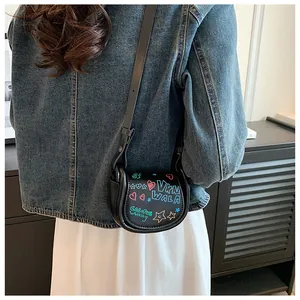 Gros plan du mini sac selle noir avec graffiti colorés et bandoulière réglable pratique