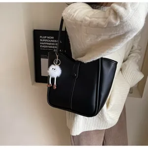 Detail of black leather tote bag featuring a cute furry monster charm with long legs