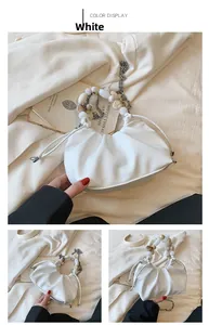 Close-up of white ruched handbag with pearl beaded handle and metal chain detail