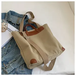 Detail of khaki canvas tote bag featuring brown leather trim and adjustable shoulder strap