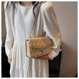 Detail of beige quilted shoulder bag with wave pattern and silver metal chain strap
