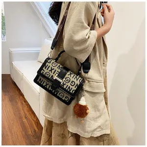 Detail of beige canvas crossbody bag with letter print, metal clasp and plush pendant