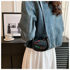 Détail d'un sac besace en cuir noir orné de motifs graffitis colorés de cœurs et d'étoiles