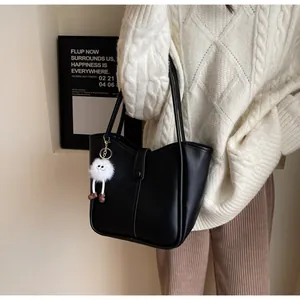 Detailed view of black faux leather tote bag featuring vertical stitching and a plush charm