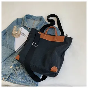 Detail of black canvas tote bag with brown leather trim and wide fabric strap accents