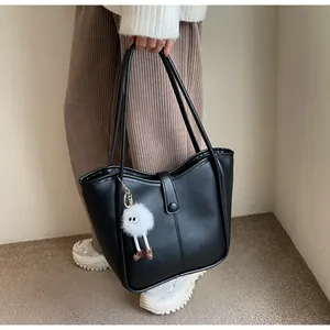 Detail view of the black tote bag featuring a cute white plush doll charm and slim straps