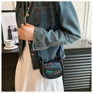 Détail d'un mini sac selle noir avec graffitis colorés porté sur une veste en jean