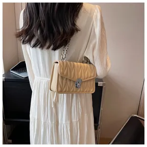 Detail of beige quilted chain bag with silver twist lock on a white pleated dress