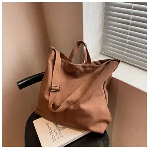 Detail of a brown canvas tote bag with adjustable shoulder strap on a black stool