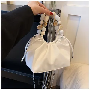 Detail view of the white pleated bag with faux pearl handle and metal chain strap