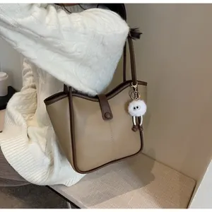 Detail of khaki tote bag with brown trim and white monster plush charm on shoulder