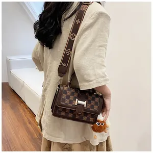 Detail view of a classic brown checkered crossbody bag with jacquard strap and plush charm