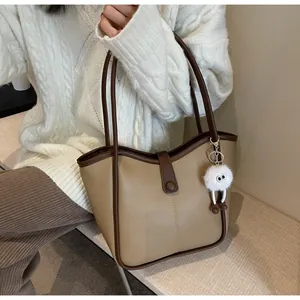 Detail of khaki tote bag with dark brown trim and a cute plush monster charm accessory