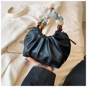 Detail of black pleated cloud bag featuring colorful resin bead handle and logo embossing
