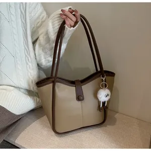 Detail of khaki tote bag with magnetic clasp and fuzzy eyeball pendant on the handle