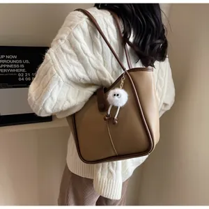 Detail of khaki tote bag with plush charm on shoulder of model in white sweater