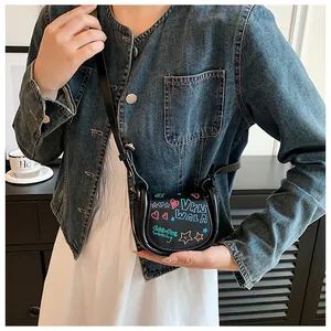 Gros plan d'un mini sac selle noir avec graffitis colorés porté par un mannequin en jean