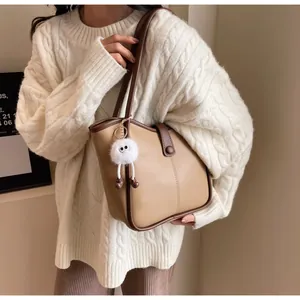 Detail of a brown patchwork tote bag with a white plush monster charm on the strap