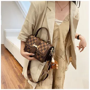 Detail of brown checkered crossbody bag with wide strap and plush pendant on model
