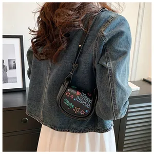 Détail d'un mini sac selle en cuir noir avec graffitis colorés et motifs de cœurs