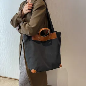 Large black canvas tote bag with brown leather trim and dual straps shown on a model