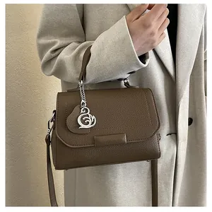 Detail of dark brown lychee pattern leather handbag with silver swan pendant and top handle