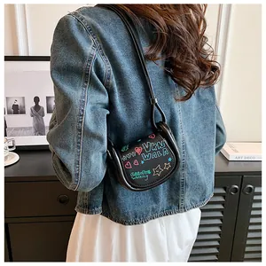 Détail d'un mini sac selle noir avec imprimés graffiti colorés et une bandoulière fine