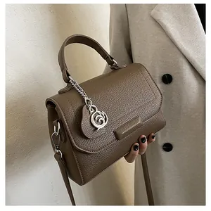 Detail view of dark brown litchi grain tote bag with silver circular pendant on beige coat