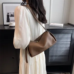 Brown leather crossbody hobo bag with wide strap styled with a white pleated dress