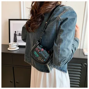 Détail du mini sac à bandoulière noir avec des motifs graffiti colorés et des étoiles