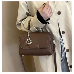 Detail showing brown pebble leather handbag with silver swan charm and top handle