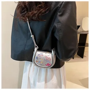 Détail d'un mini sac selle argenté avec graffitis et bord métallique sur un mannequin