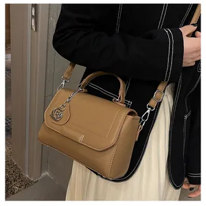 Detail of khaki pebbled leather handbag with adjustable strap and silver logo pendant