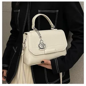 Close-up of beige lychee grain leather handbag featuring a silver swan pendant