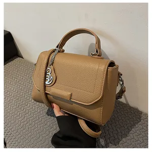 Detailed close-up of khaki pebbled leather handbag with silver floral charm and top handle