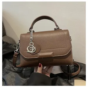 Macro view of brown lychee grain leather bag showing the silver bird pendant and texture