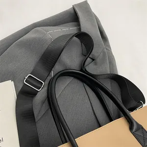 Detail of beige tote bag with black handles and adjustable nylon strap on a gray suit