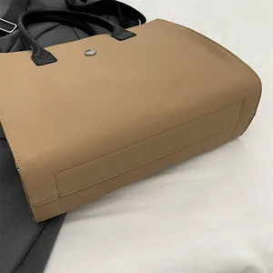 Close-up of khaki tote bag with black handles, metal buckle, and reinforced stitching
