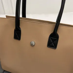 Detail of light brown tote bag featuring reinforced black leather handles and magnetic buckle