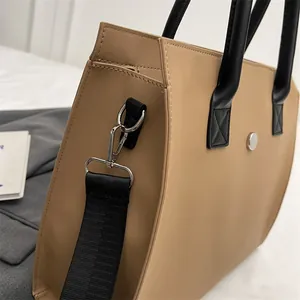 Detail of khaki tote bag showing thick nylon texture, black handles, and silver metal hardware