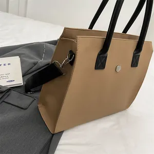 Detailed shot of beige tote bag with black handles and detachable woven strap on soft linen