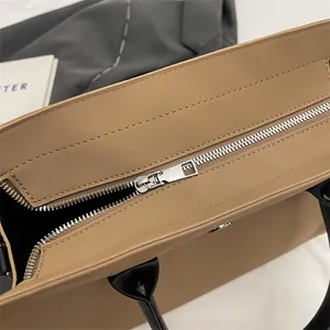 Detail view of the smooth metal zipper closure and black leather handles on a khaki tote bag