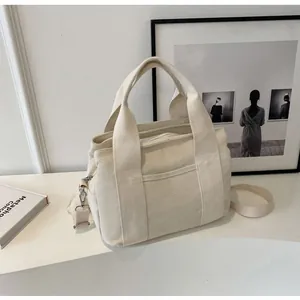 Cream canvas tote with wide handles and adjustable strap shown in a minimal indoor setting
